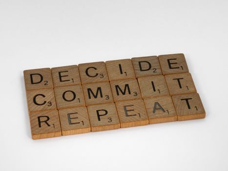 Wooden letter tiles display the motivational phrase 'Decide, Commit, Repeat' on a plain background.